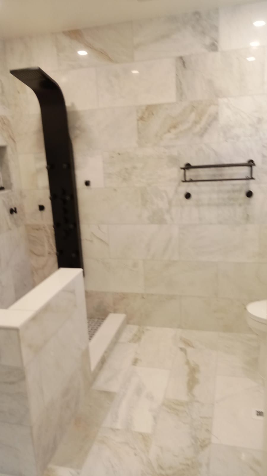 Marble-tiled bathroom with walk-in shower, black arched shower fixture, and towel bars