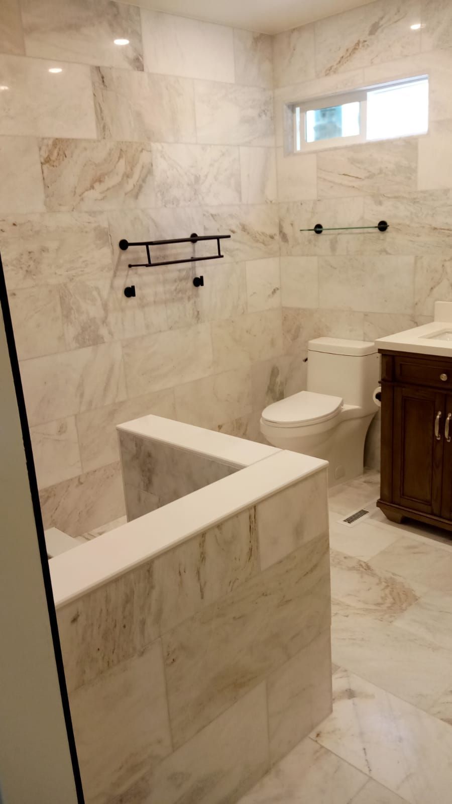Marble bathroom with walk-in tub, toilet, vanity, and towel bars under a small window