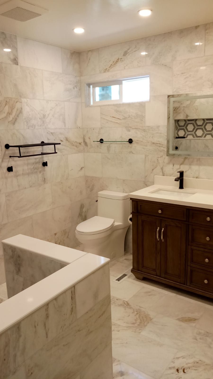 Marble bathroom with bathtub, toilet, vanity, window, and black towel bars