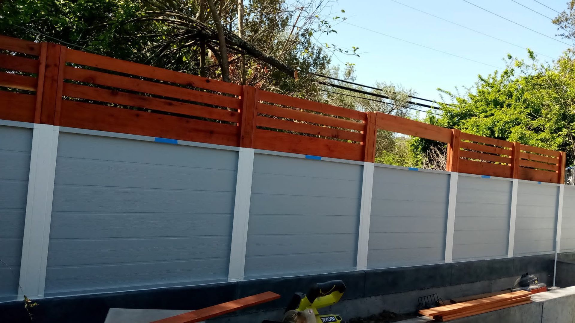 Concrete fence with gray panels and orange slats under a clear sky, beside a street.