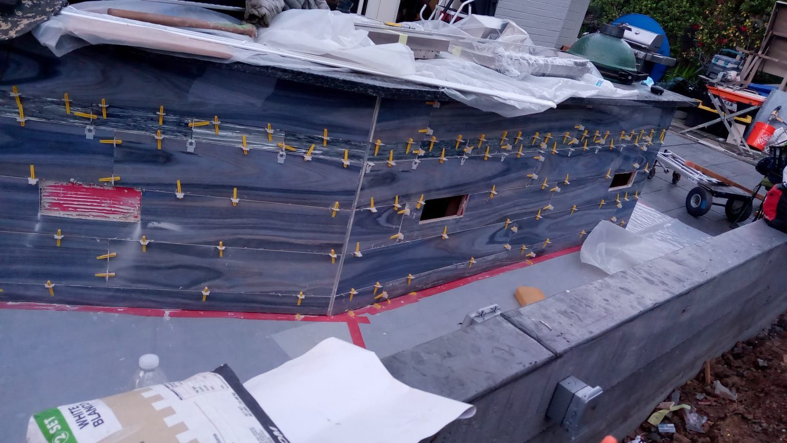 Damaged dark-blue boat hull under repair, with workers and tools on a docked vessel.