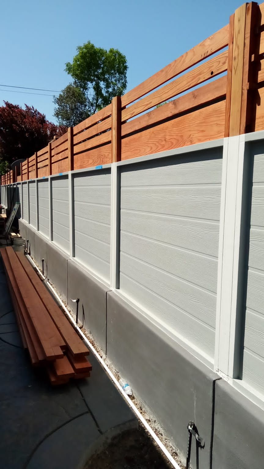 White fence with orange slats above it, shown along a narrow side yard in sunlight.