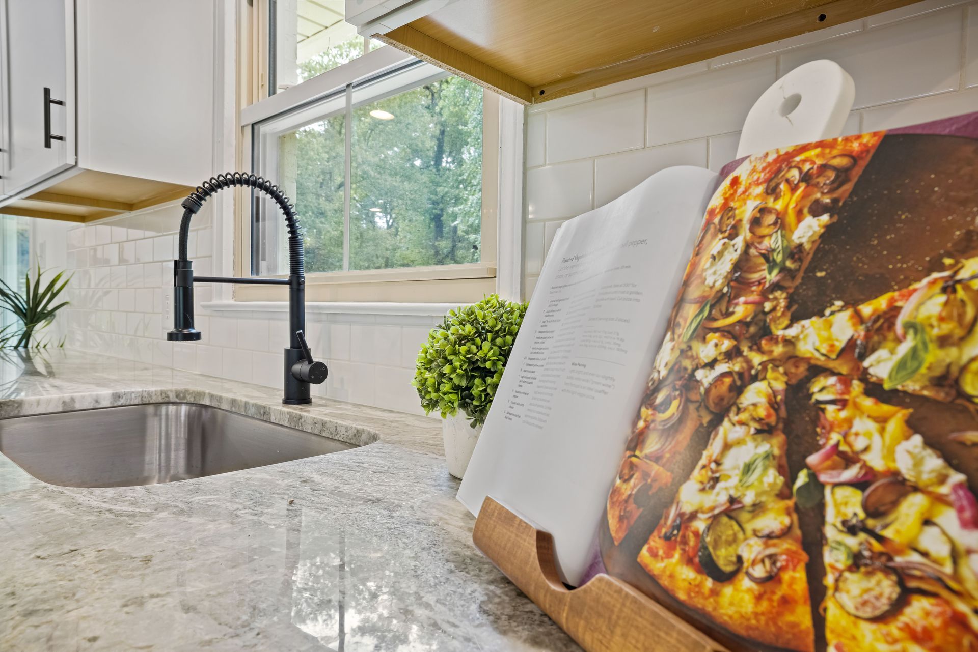 Modern kitchen counter with sink, black faucet, and a cookbook on a wooden stand