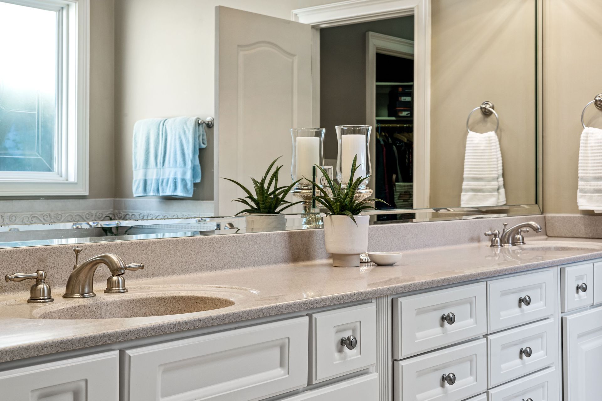 Bright bathroom vanity with double sinks, beige countertop, and a mirror reflecting towels and a closet.