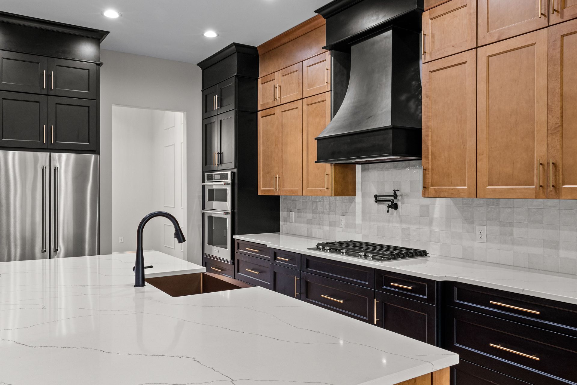 Modern kitchen with white island, black and wood cabinets, stainless fridge, and black range hood
