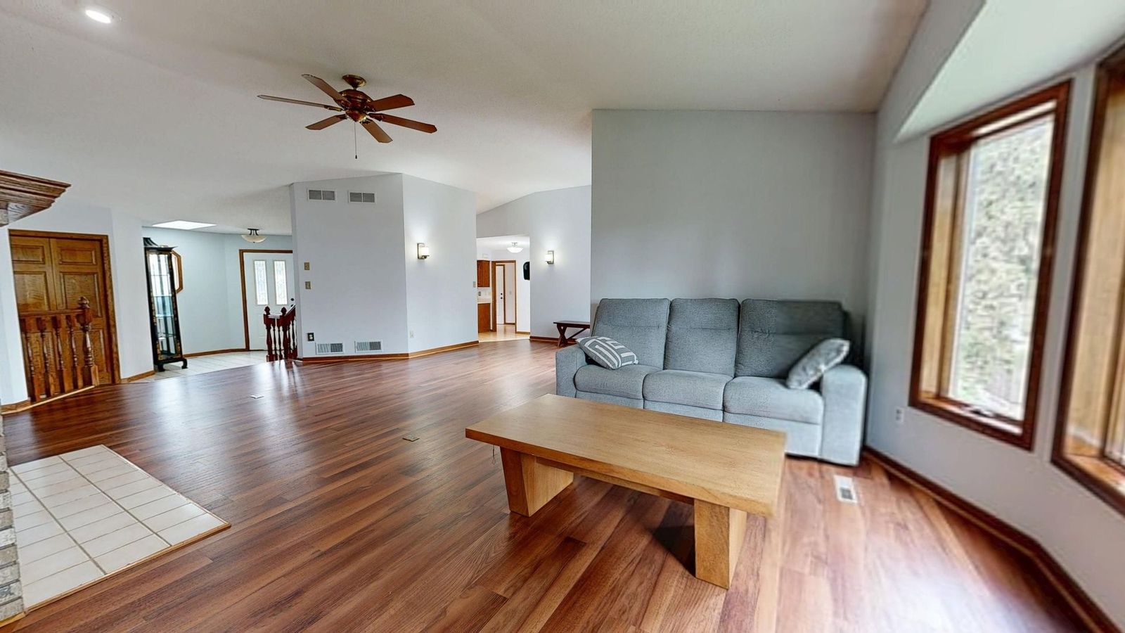 Bright living room with gray sofa, wooden coffee table, hardwood floor, and large windows