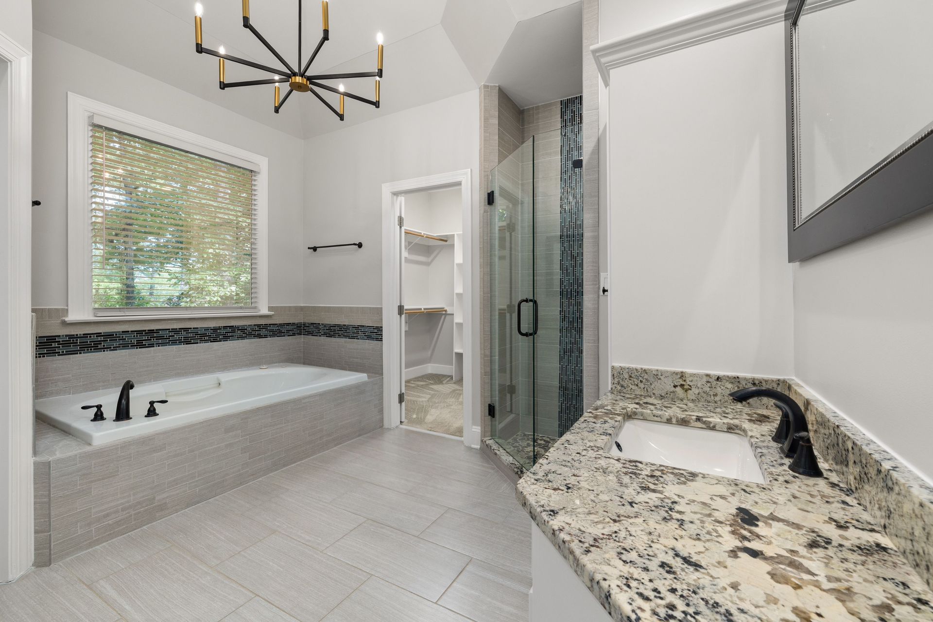 Bright modern bathroom with a soaking tub, glass shower, granite vanity, and large window.