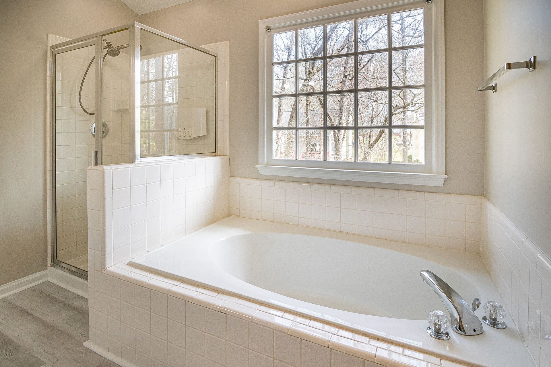 Bright white bathroom with a bathtub, glass shower, and large window.