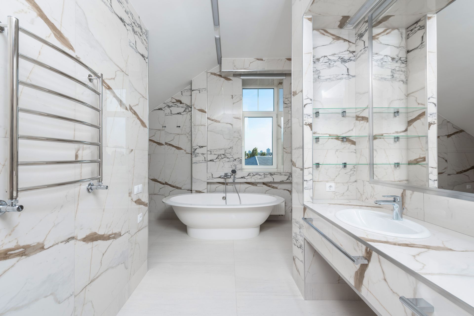 Modern white marble bathroom with a freestanding tub, glass shower, and towel warmer