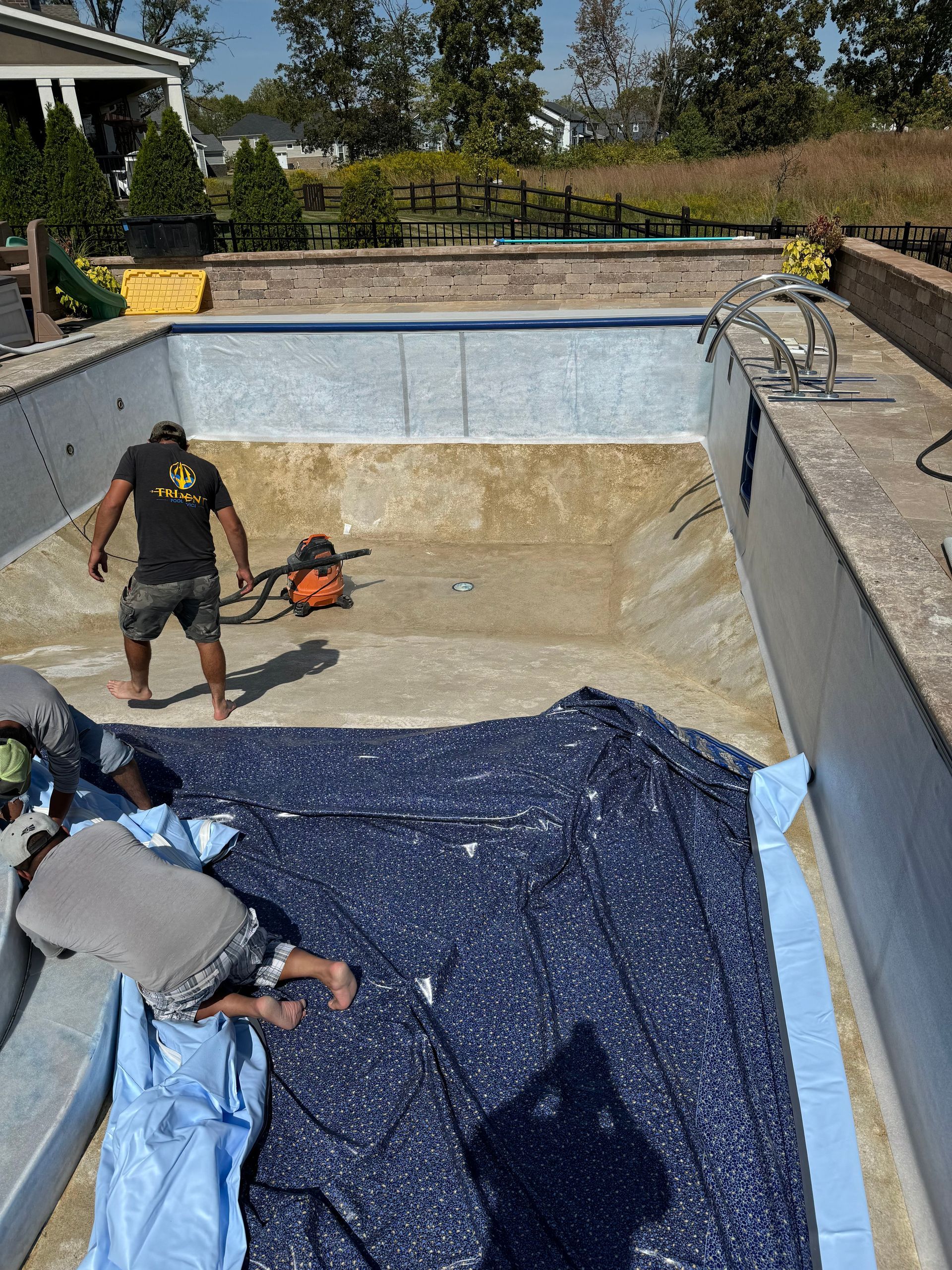 Workers cleaning a drained swimming pool with hoses and tarps.