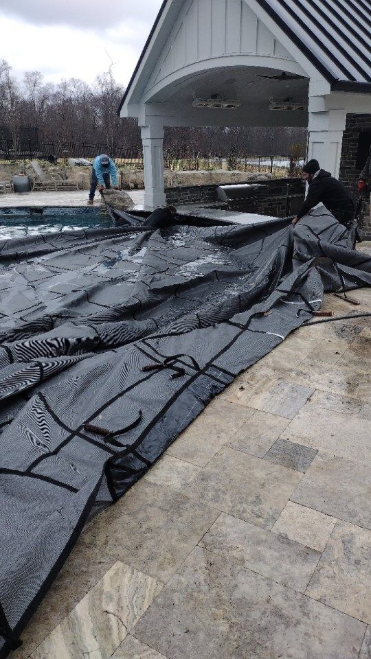 Workers installing black roofing underlayment on a house porch roof during repairs