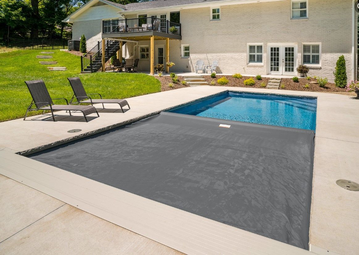 Backyard pool with a gray safety cover, lounge chairs, patio, and a house in the background