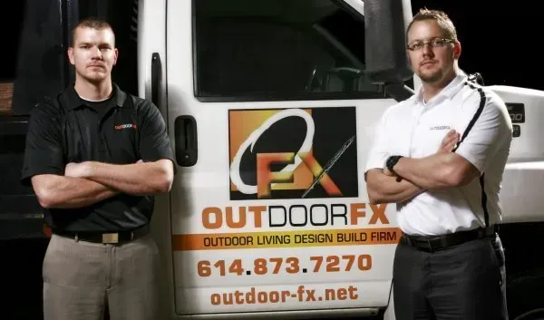 Two men stand beside an Outdoor FX truck with logo and contact info on the side.