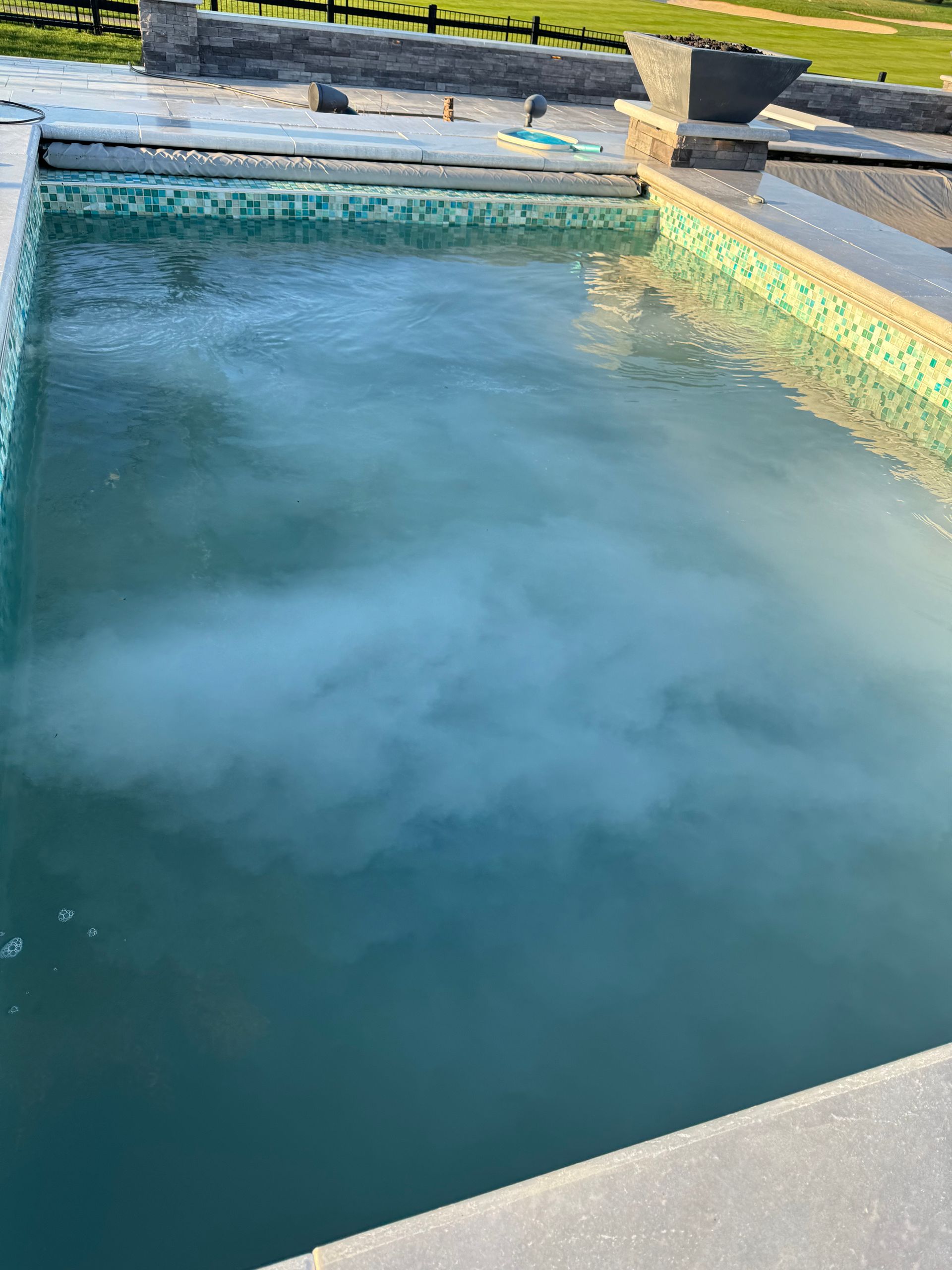Cloudy blue pool water with a misty patch near the surface, bordered by turquoise tile and concrete deck.