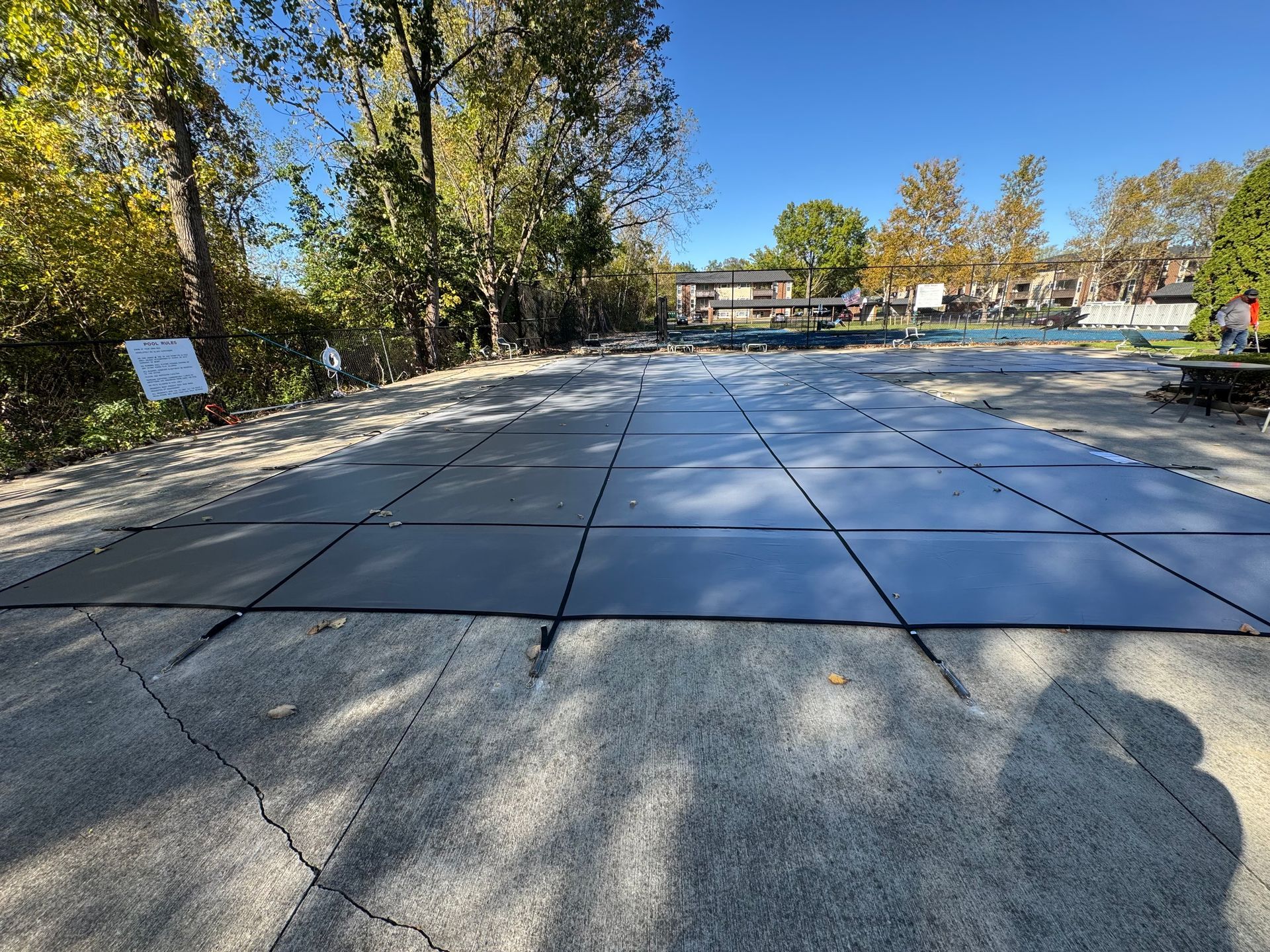Large paved plaza with low stone slabs, trees on both sides, and a small sign in the distance under a blue sky