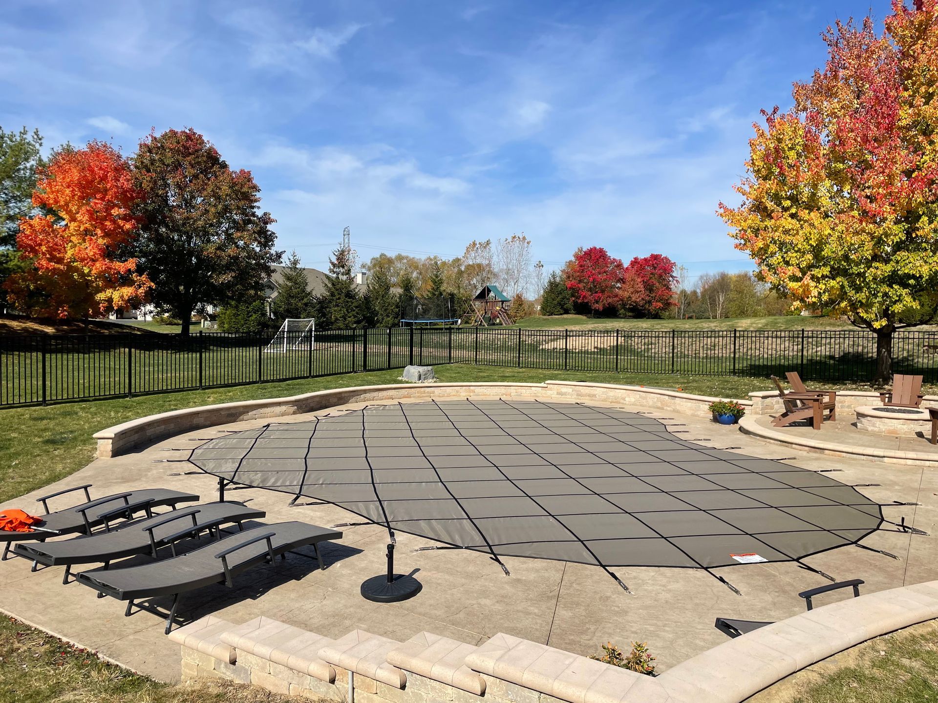 Backyard patio with outdoor furniture, stone pavers, and autumn trees under a blue sky