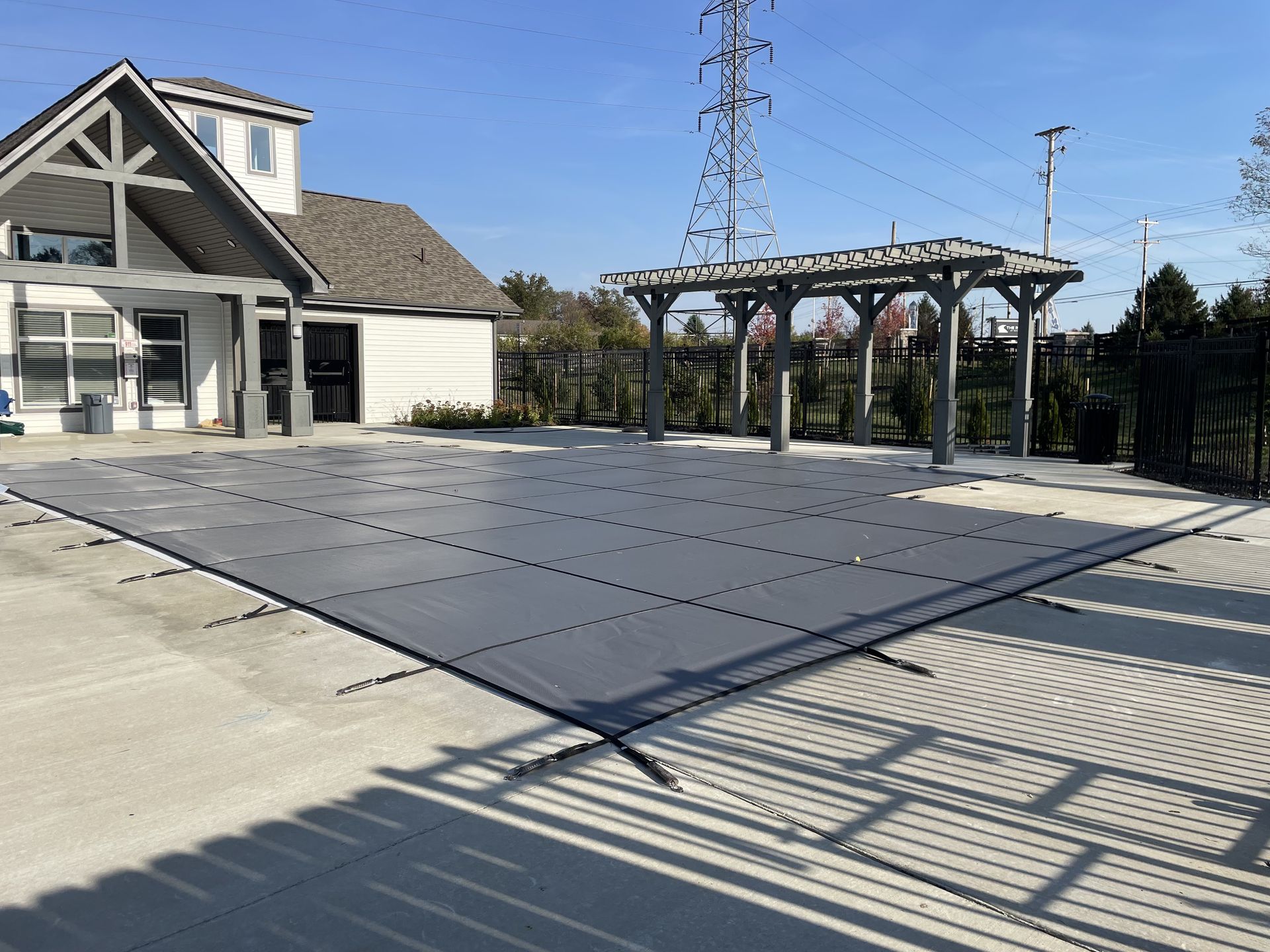 Backyard patio with dark paver surface, pergola, house, and fence in bright sunlight