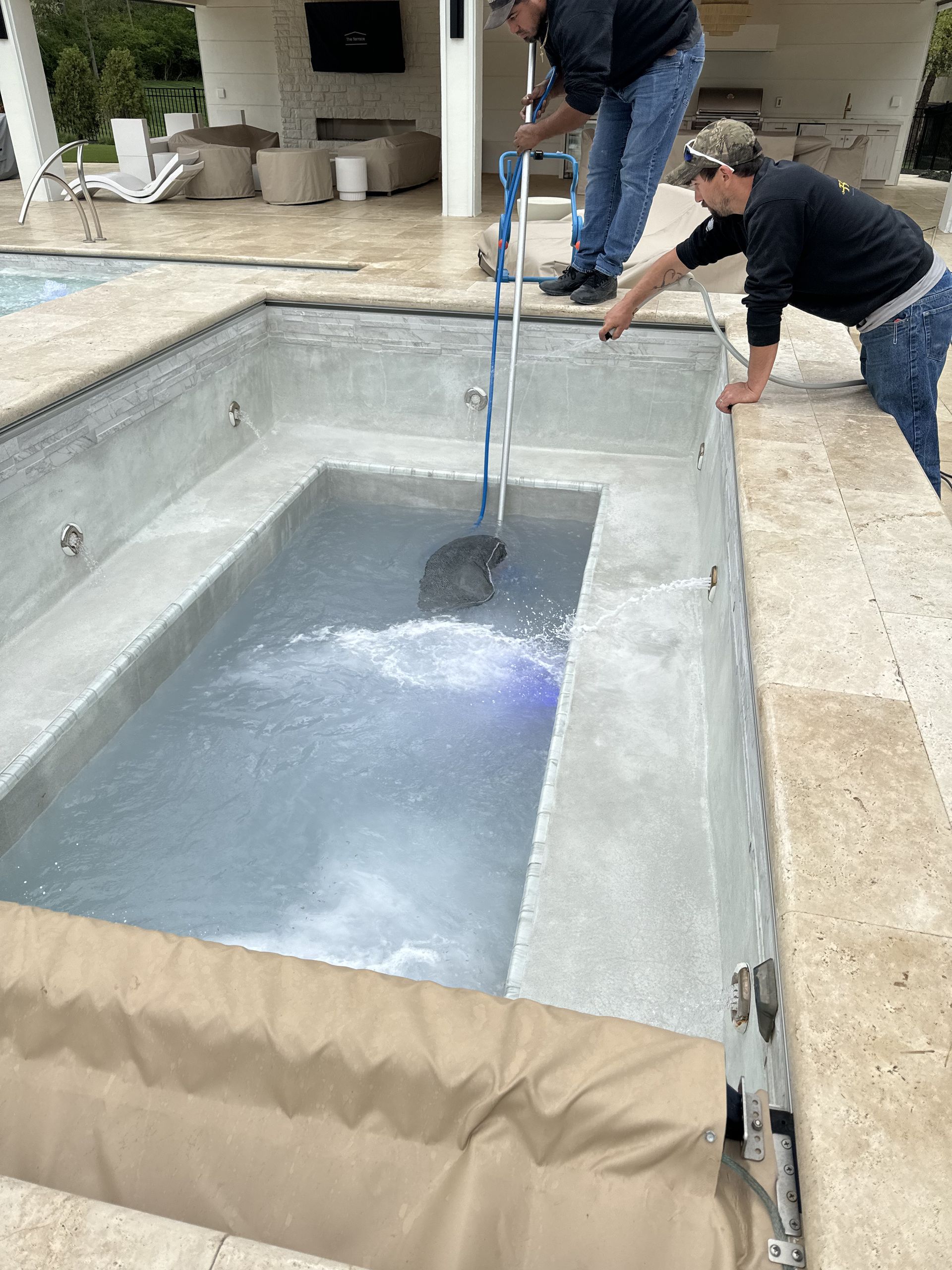 Two workers testing a rectangular pool with a hose and water inside.