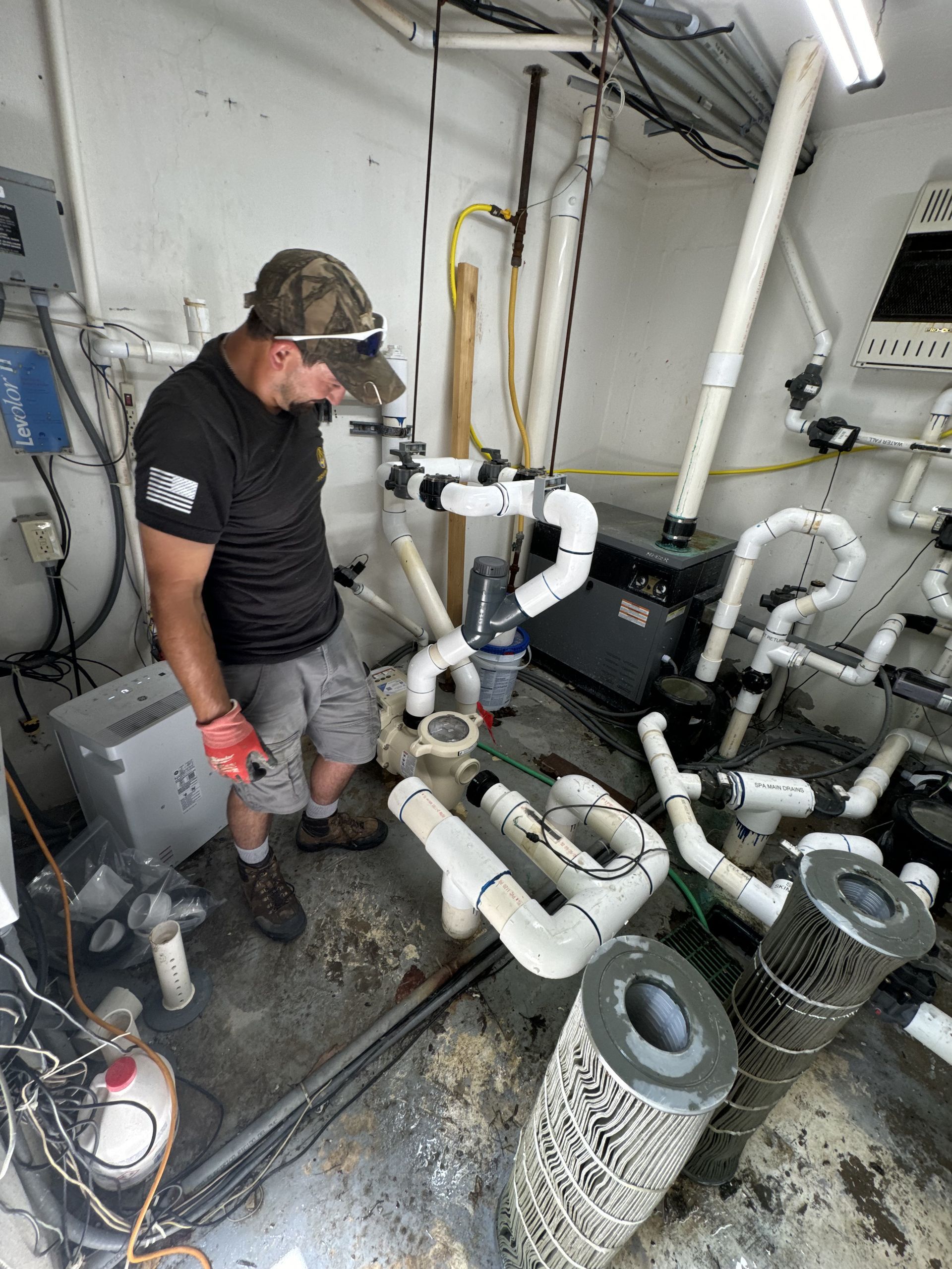 Worker inspecting pool plumbing and filter equipment in a mechanical room
