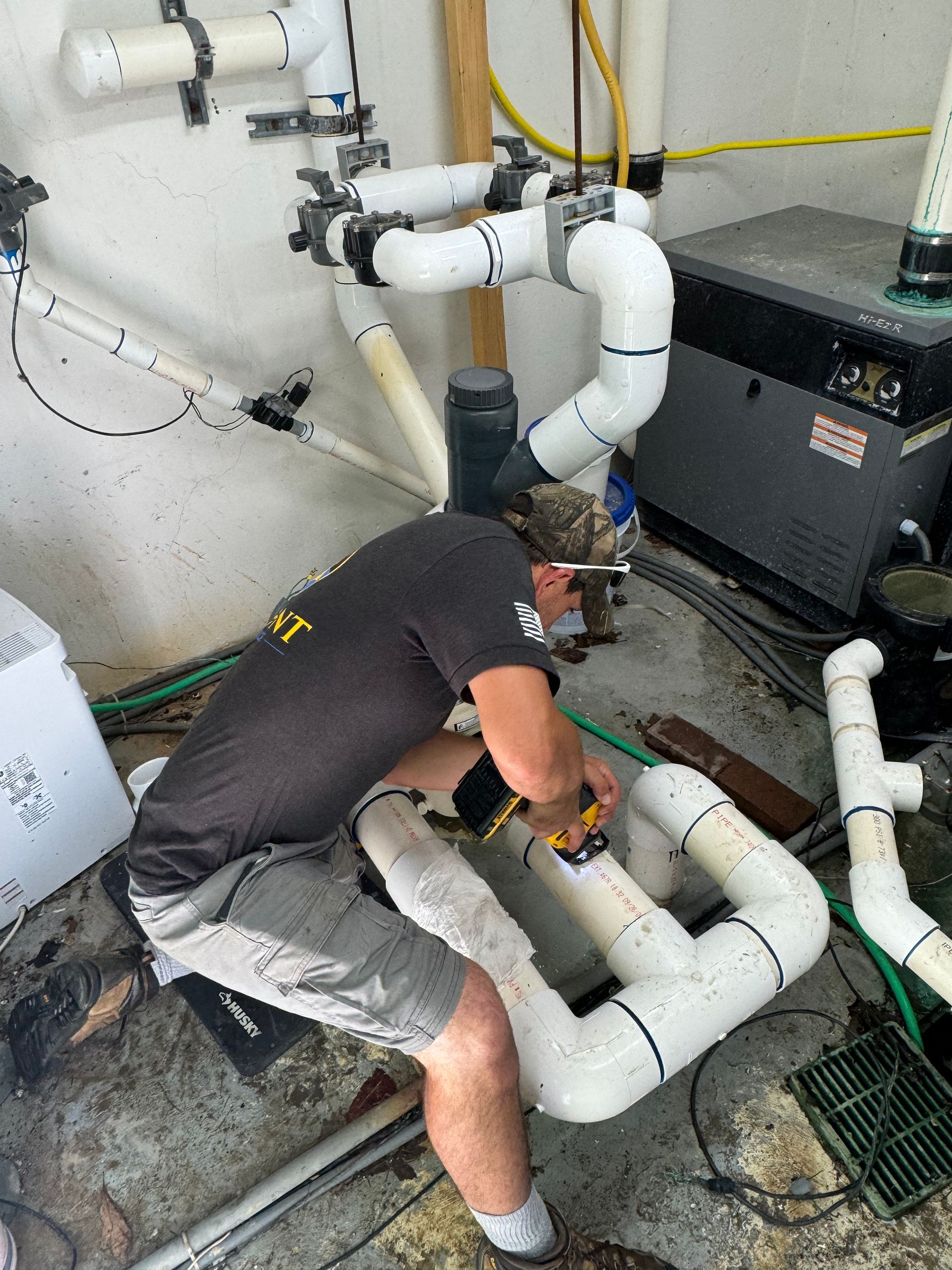 Person working on white PVC pipes in a utility room with tools and machinery.