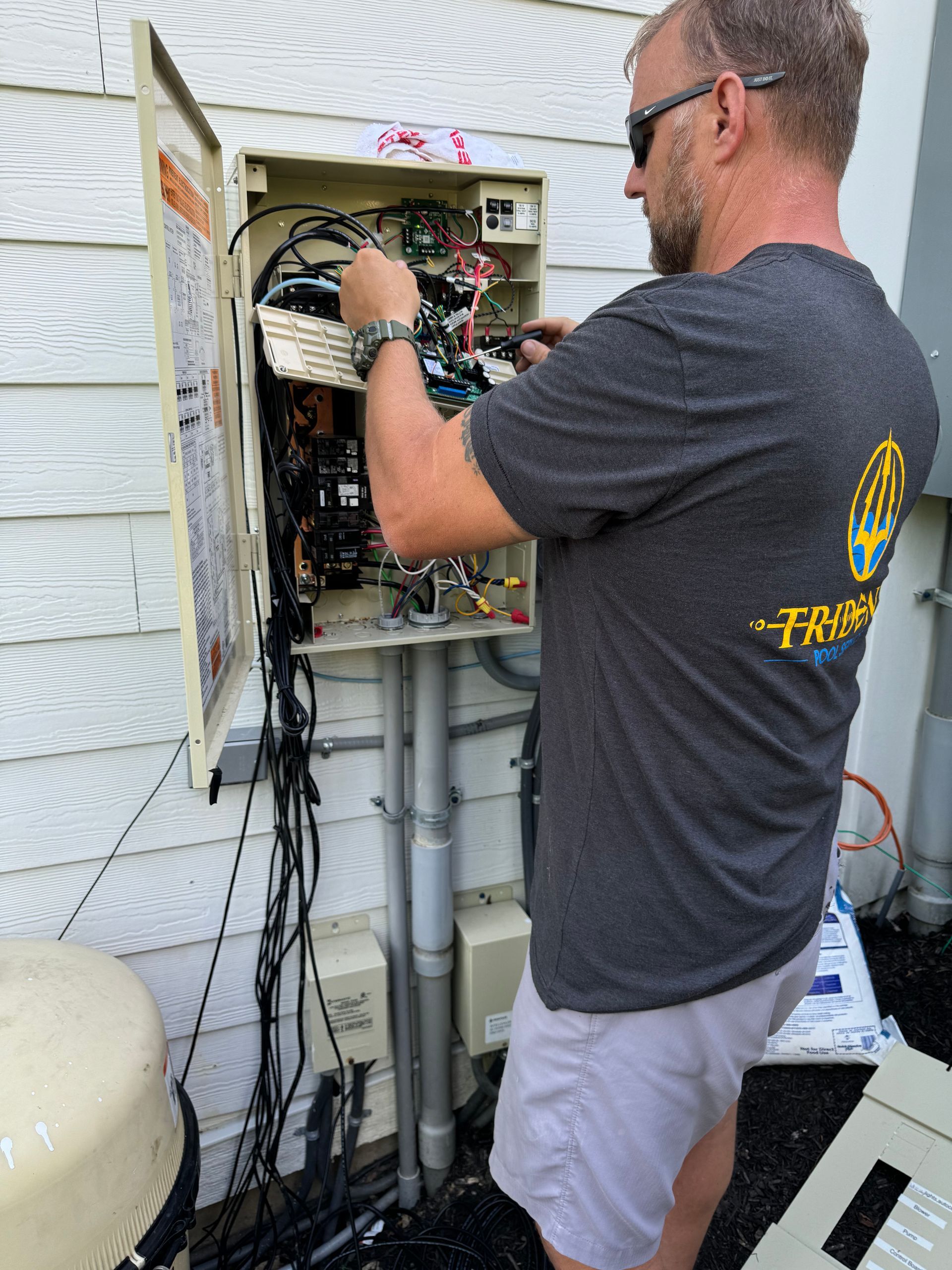 Technician repairing an open electrical panel outside a house, with wiring and equipment exposed.