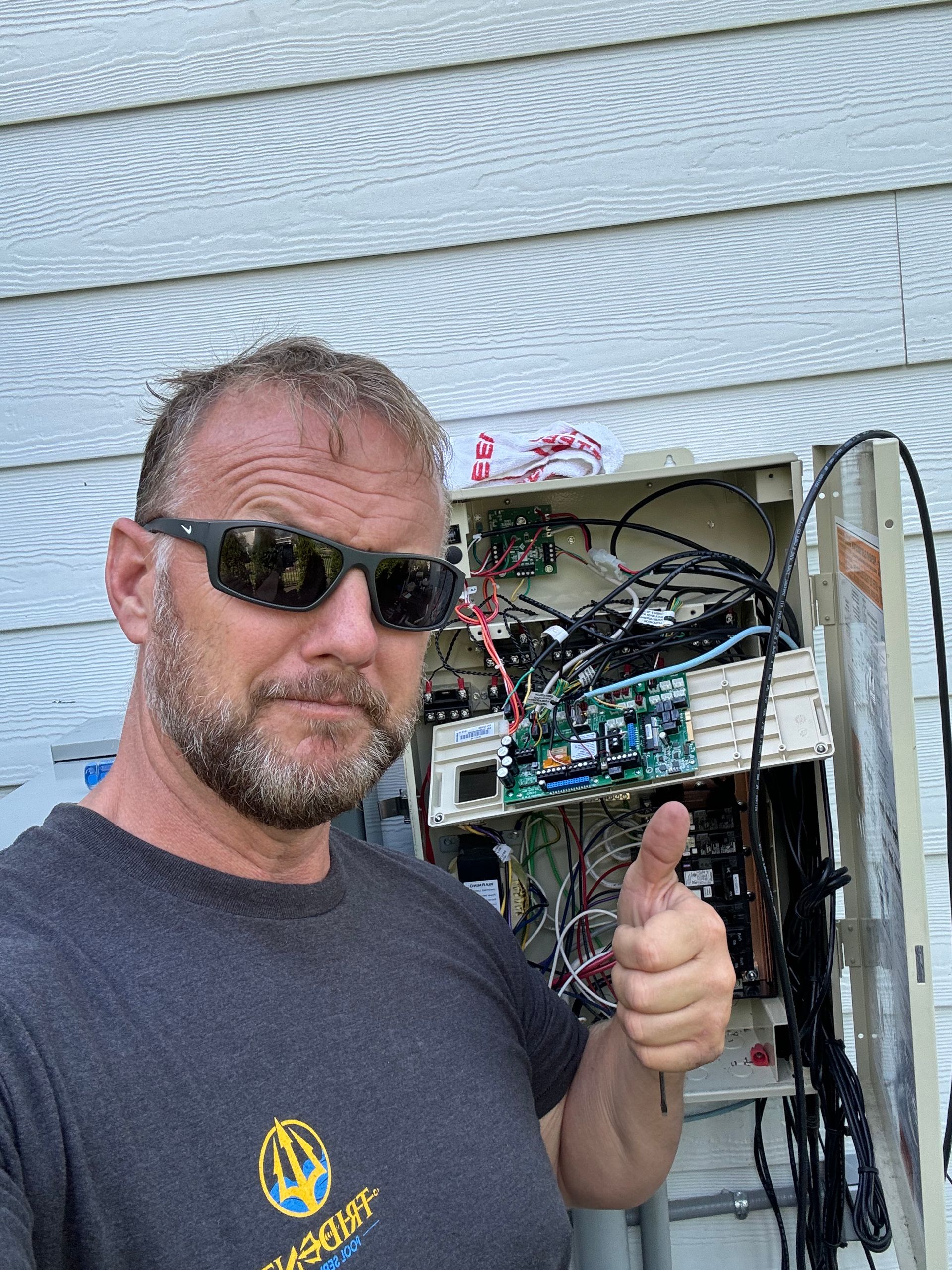 Man in sunglasses giving a thumbs up beside exposed electrical wiring and equipment outdoors