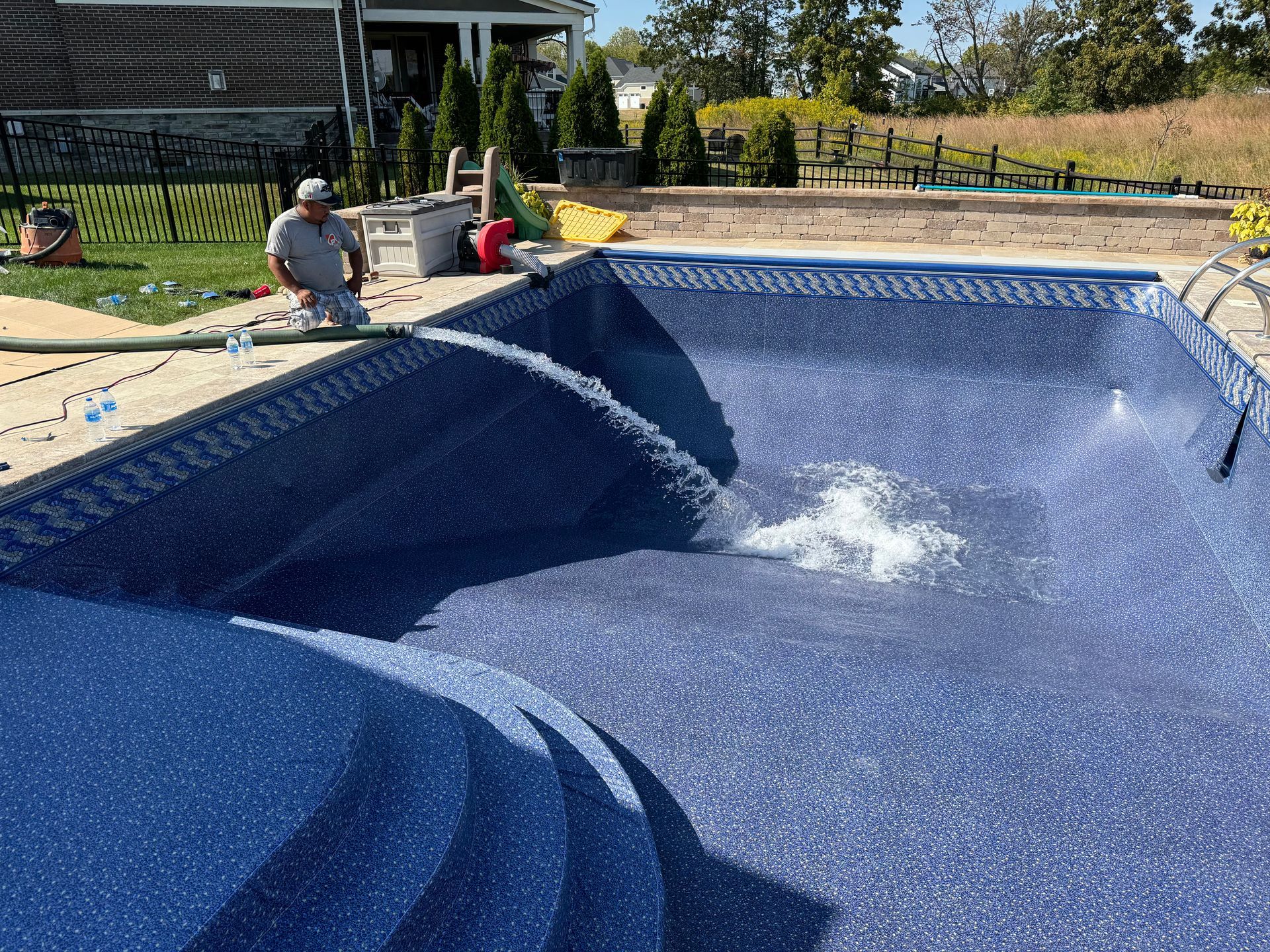 Blue swimming pool under construction with a worker spraying water inside the liner