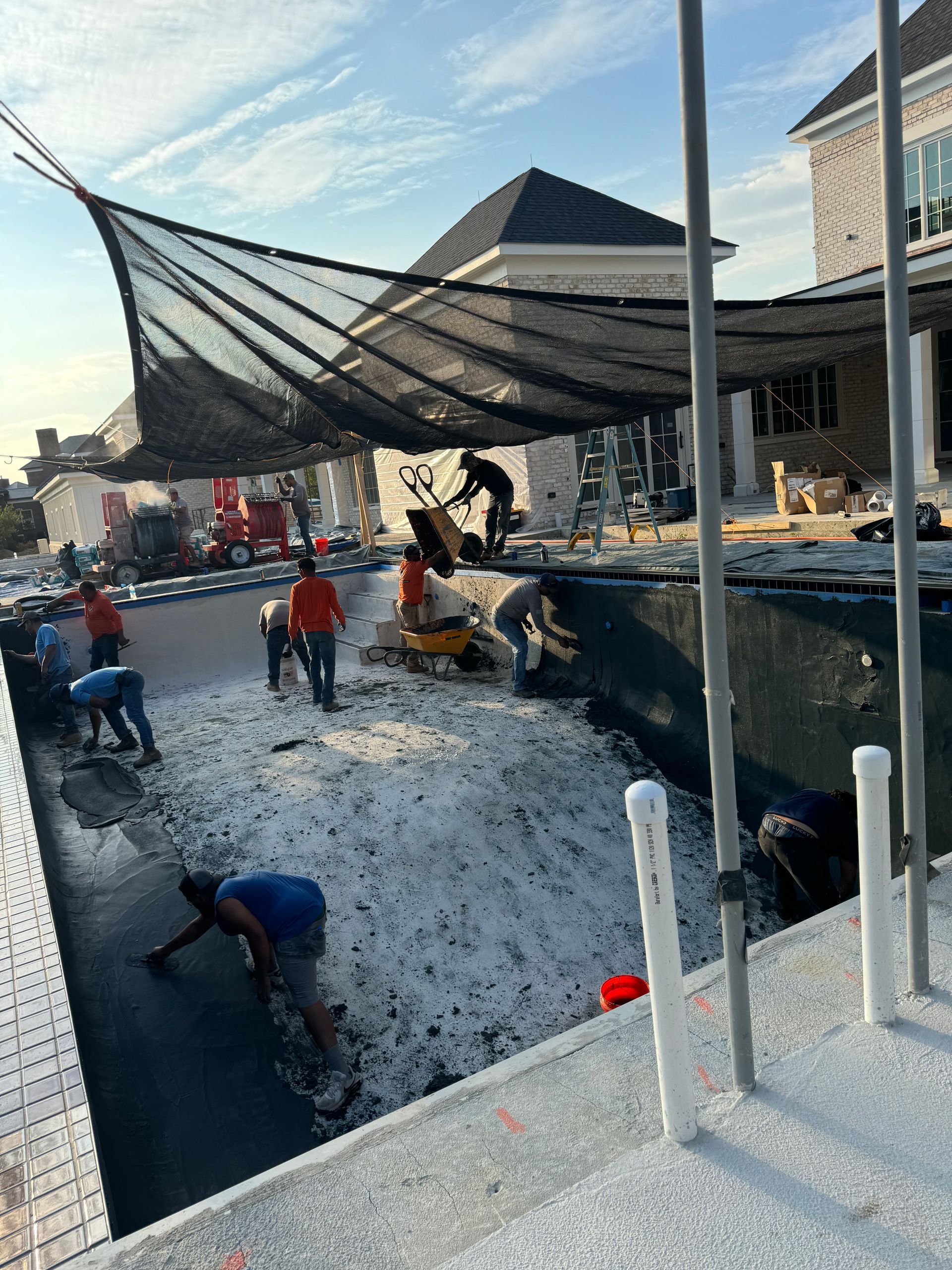 Workers spreading white material under a large black canopy in a construction yard
