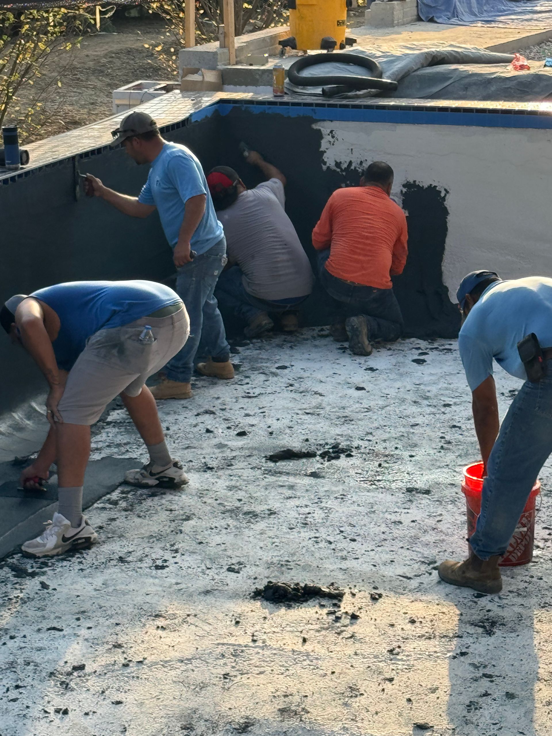 Workers repairing a road in a black asphalt patch, kneeling and smoothing the surface with tools.
