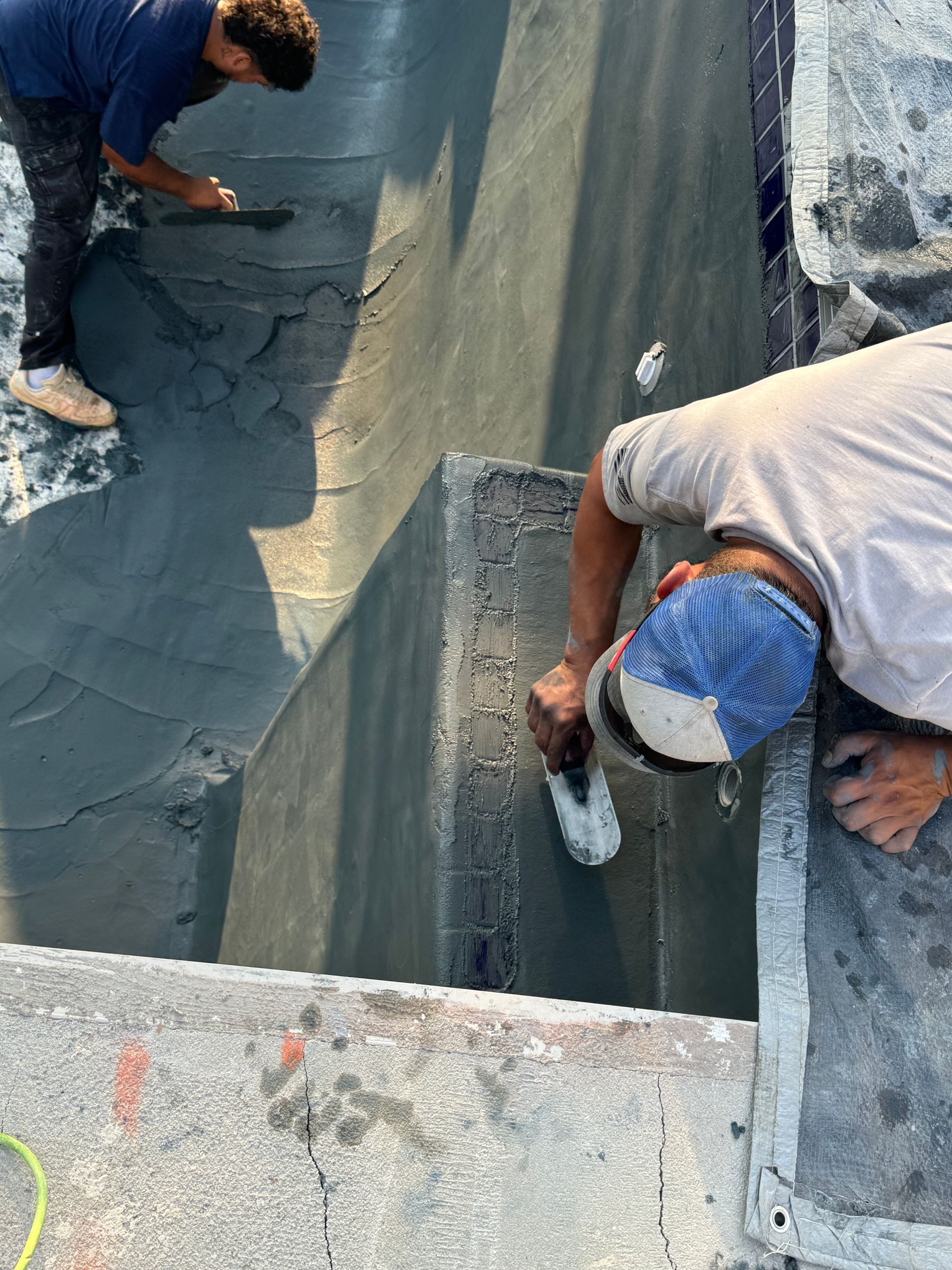 Two workers applying gray coating inside a concrete trench