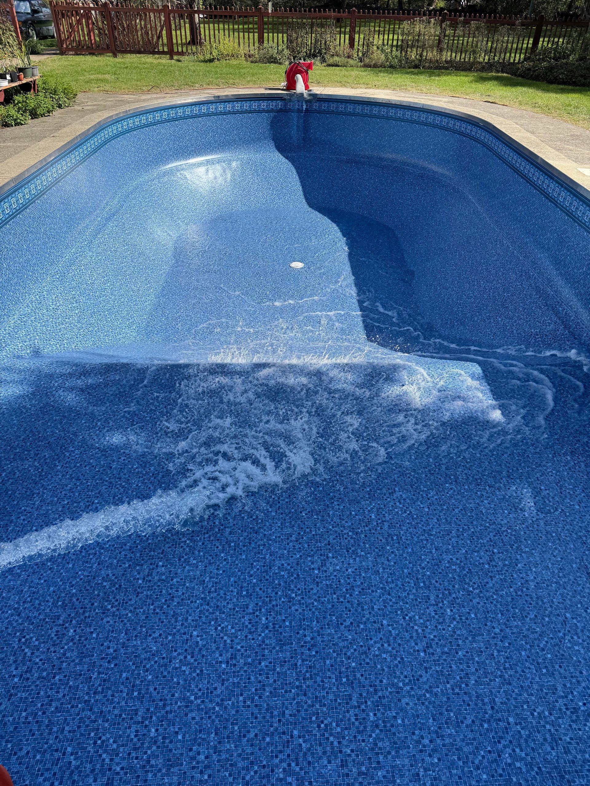Empty blue swimming pool with a red pool vacuum hose and sunny outdoor deck