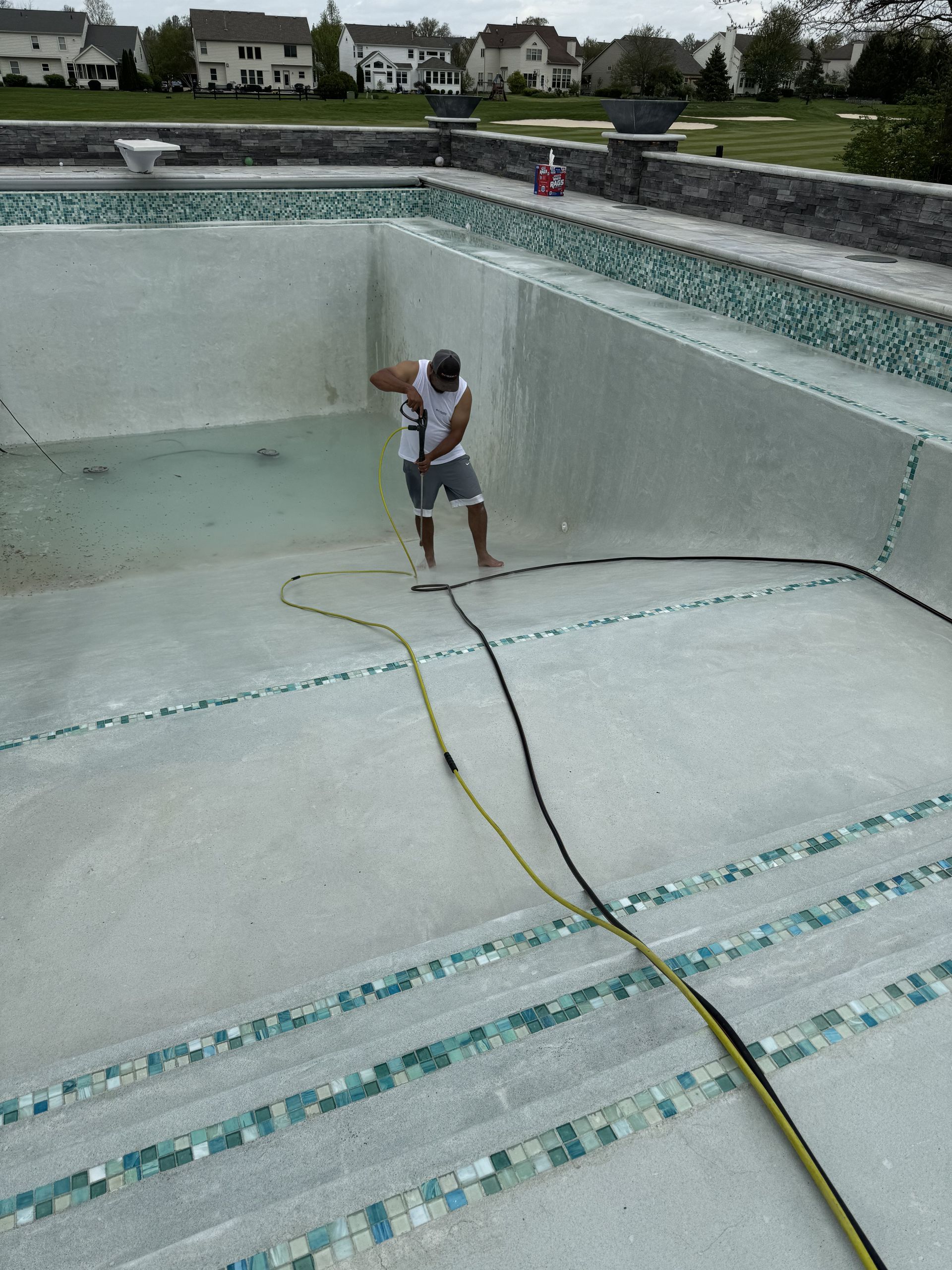 Person standing in an empty pool, holding a hose in a light gray concrete basin.