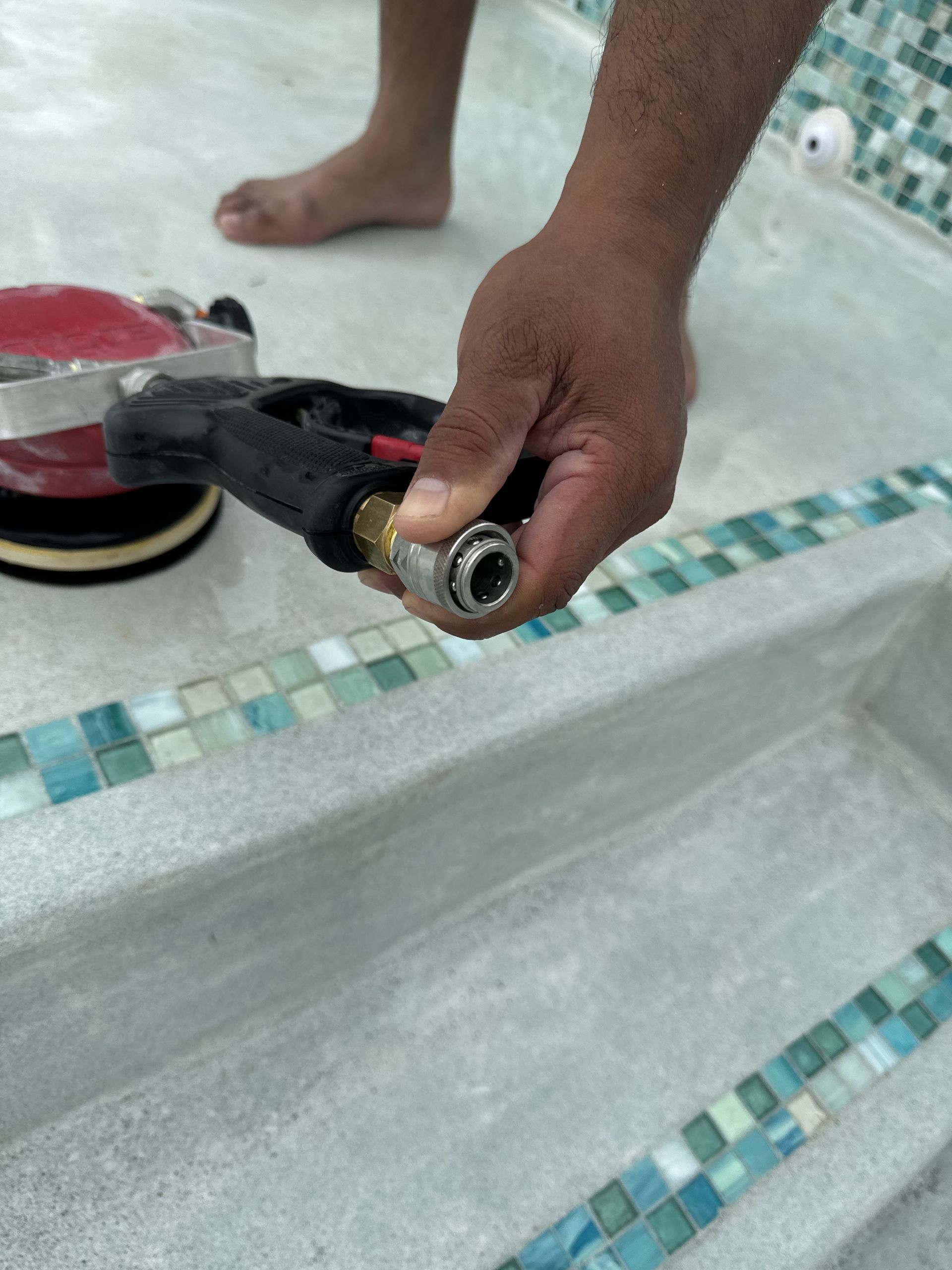 Hand holding a power tool with a spinning pad beside a tiled bathtub surface