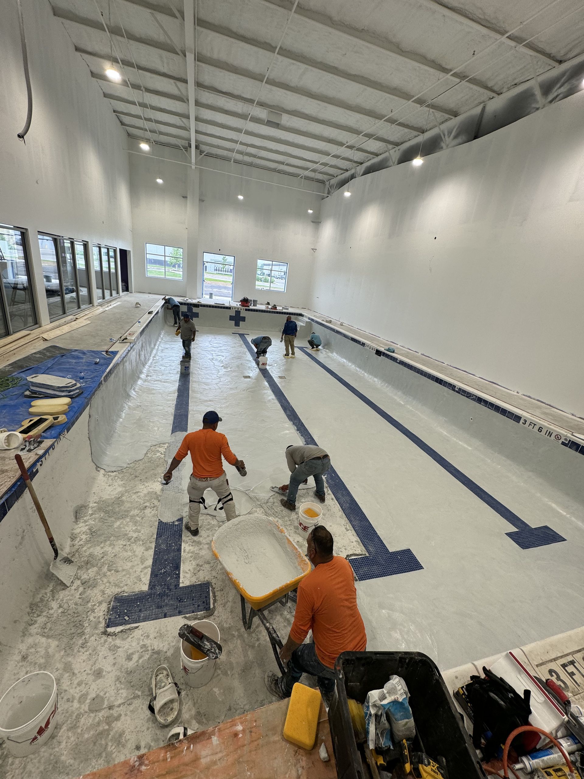 Workers laying blue lines in an indoor swimming pool under construction