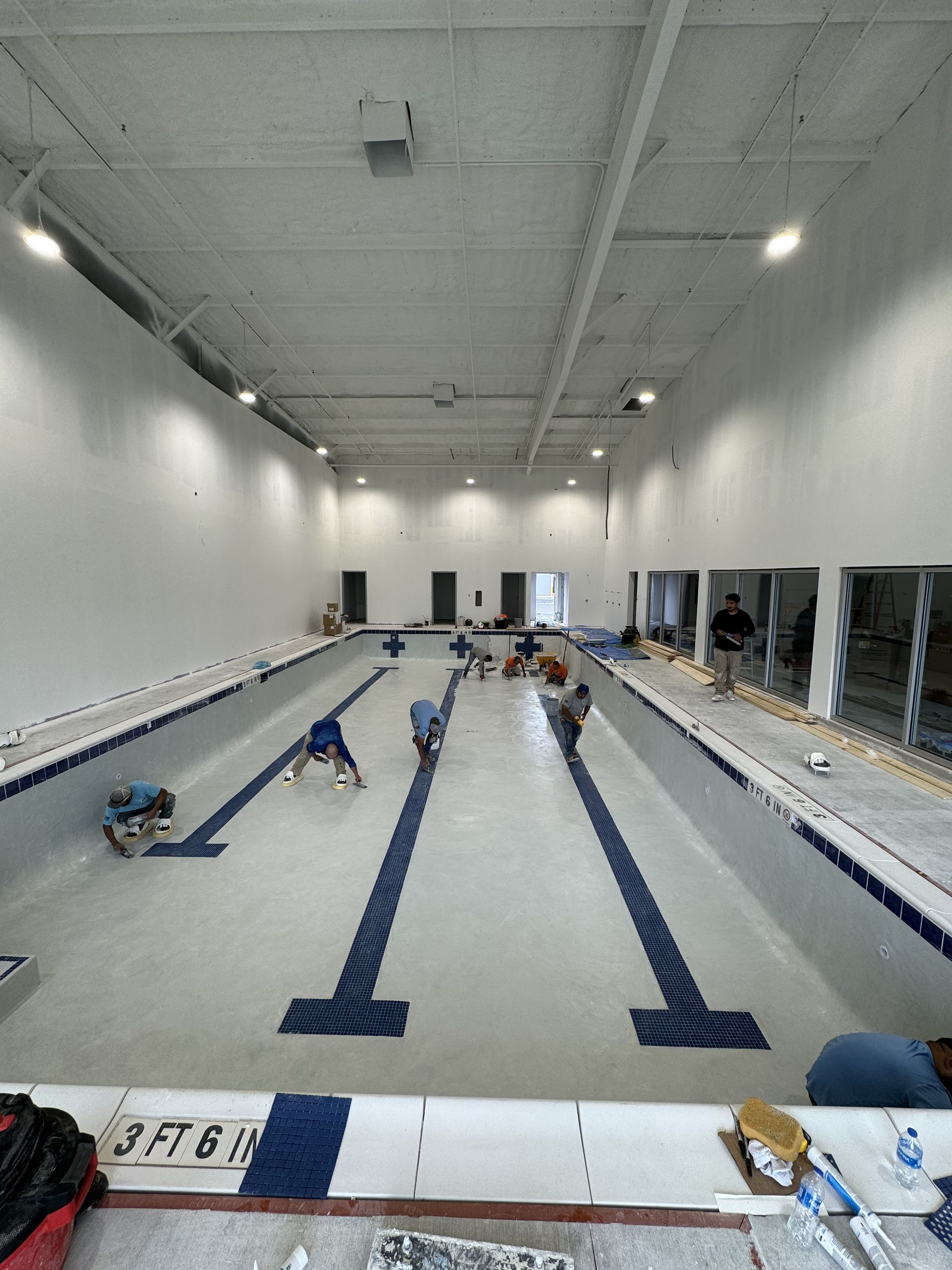 Indoor pool under construction with workers, blue lane markers, and white walls