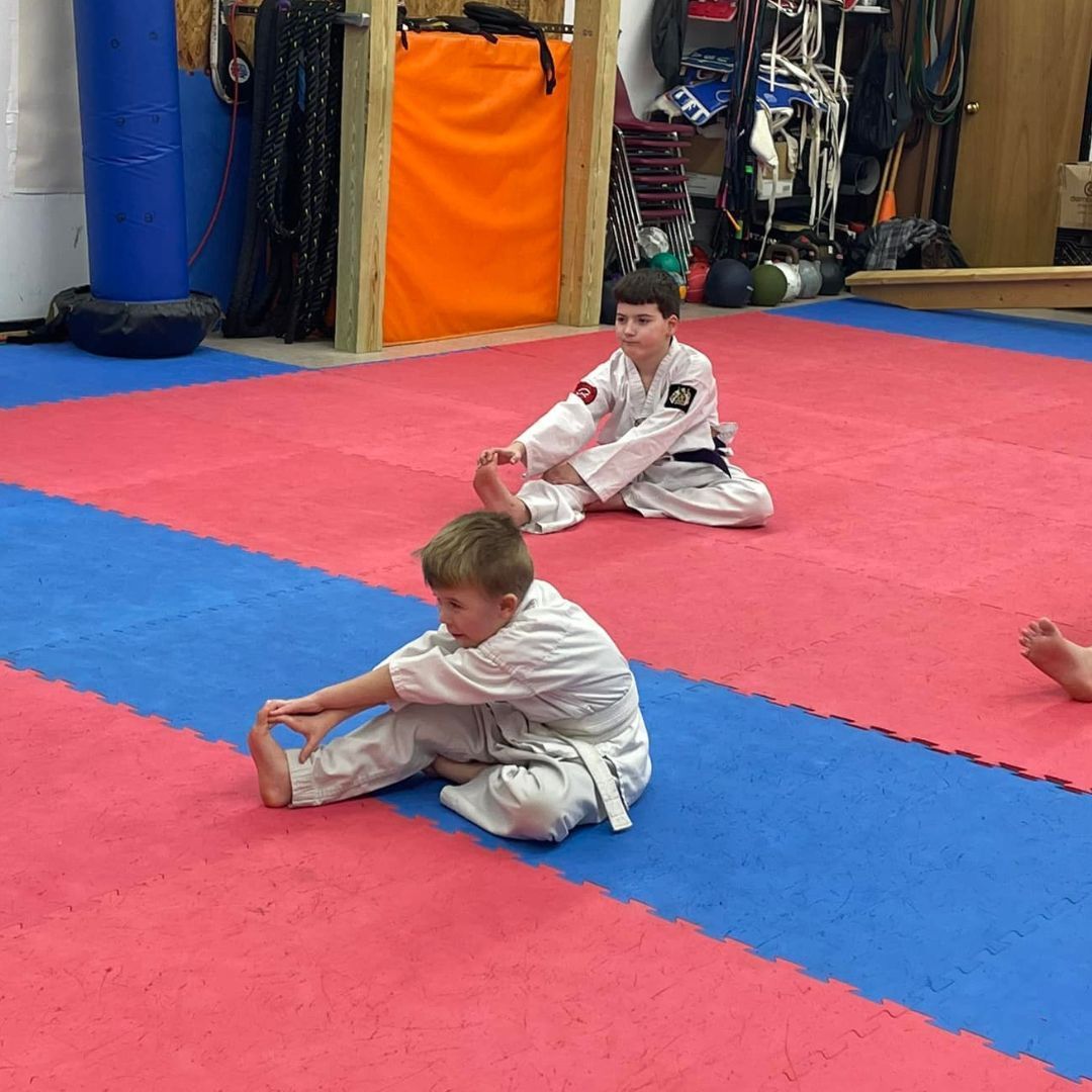A young girl in a karate uniform is sitting on the floor.
