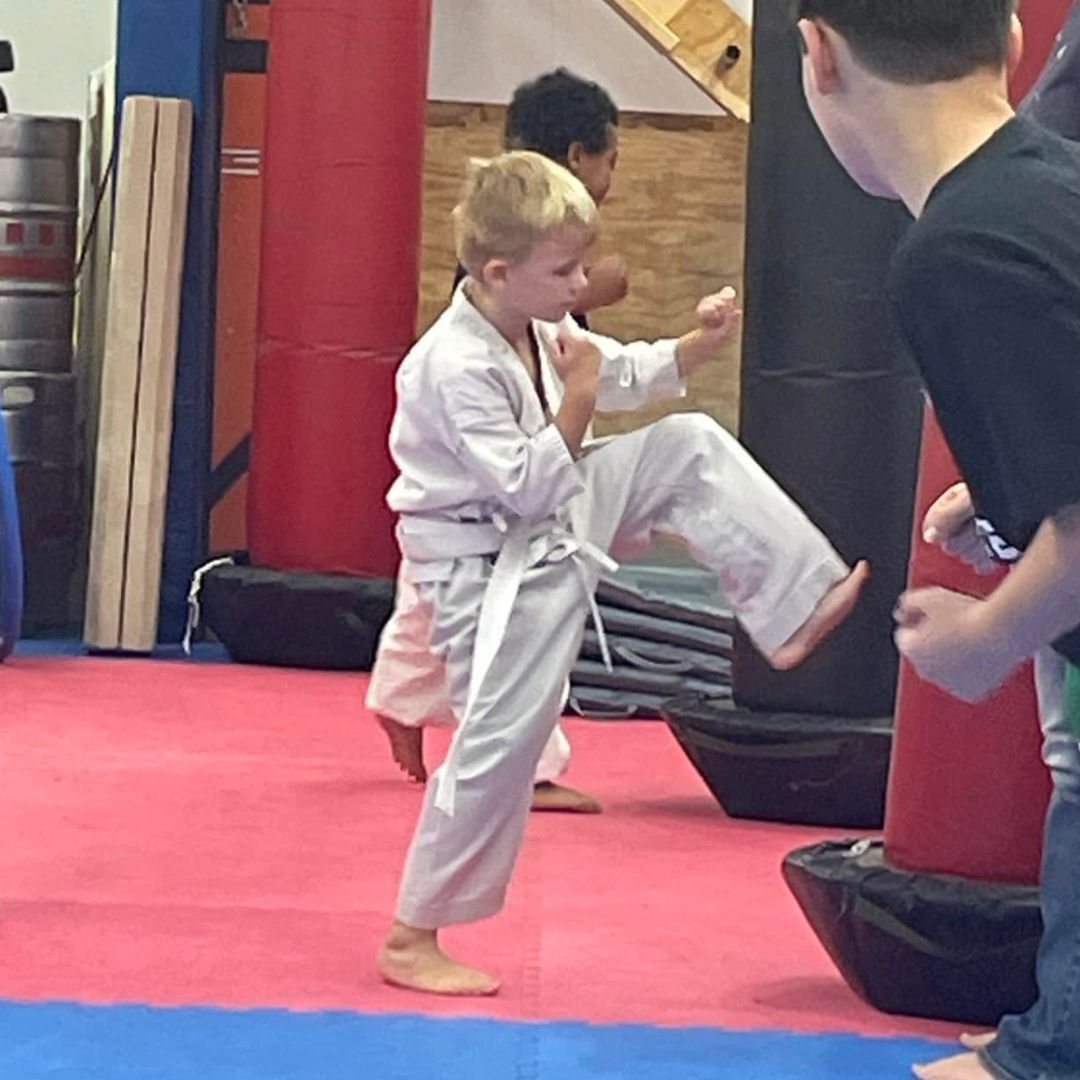 A group of children are practicing karate with a teacher in a gym.
