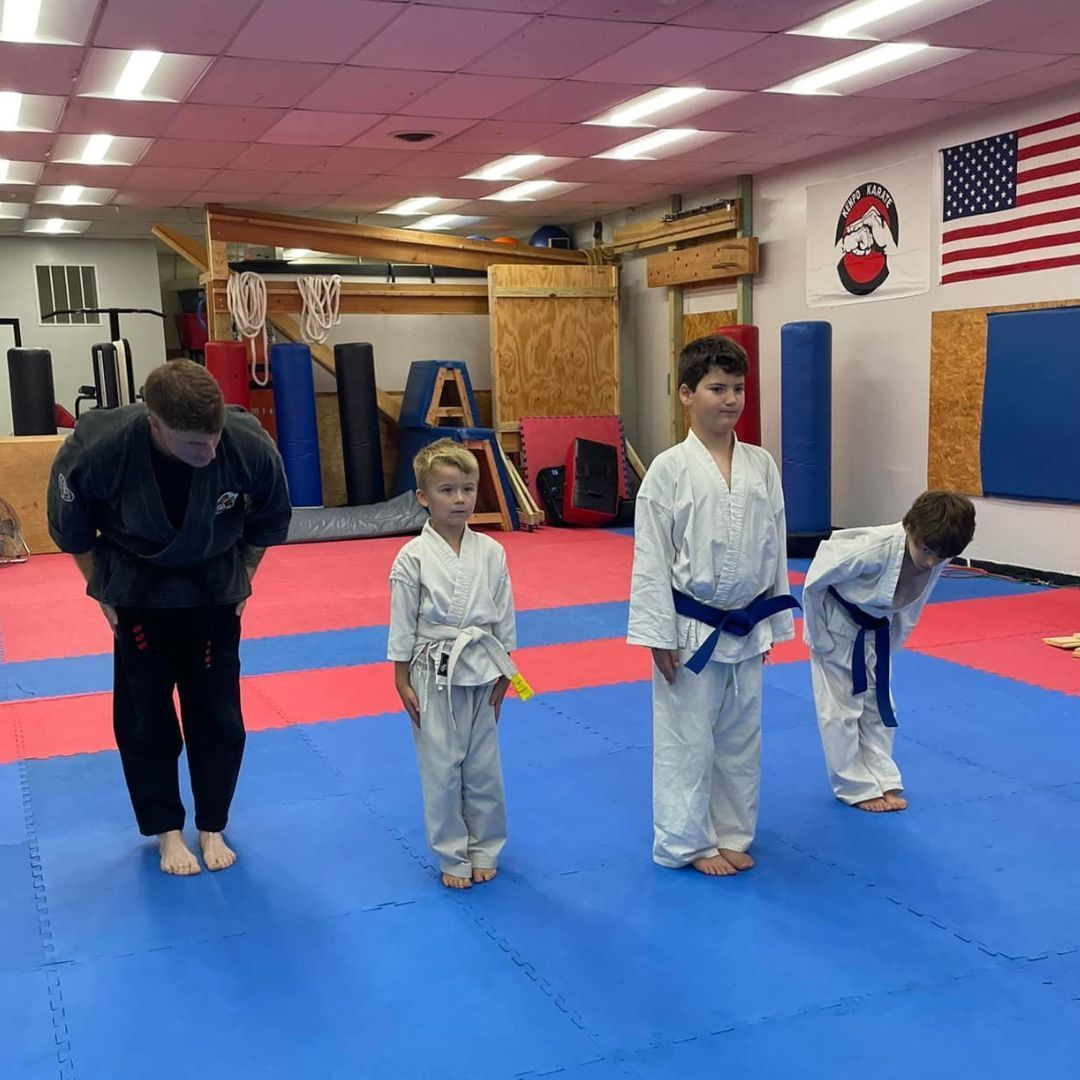 A man is kneeling down next to a young boy in a taekwondo class.