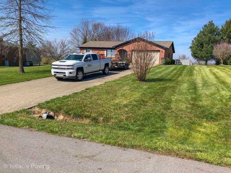 A white pickup truck with a trailer parked in the driveway of a brick house with a large, neatly mowed lawn.