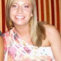 Blonde woman smiles, wearing a floral one-shoulder top. Red and white striped backdrop.