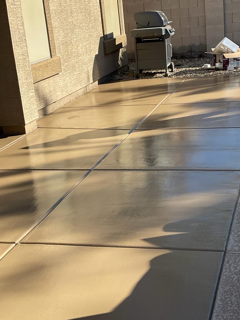A shiny, newly sealed concrete patio with visible grout lines and a grill in the background.