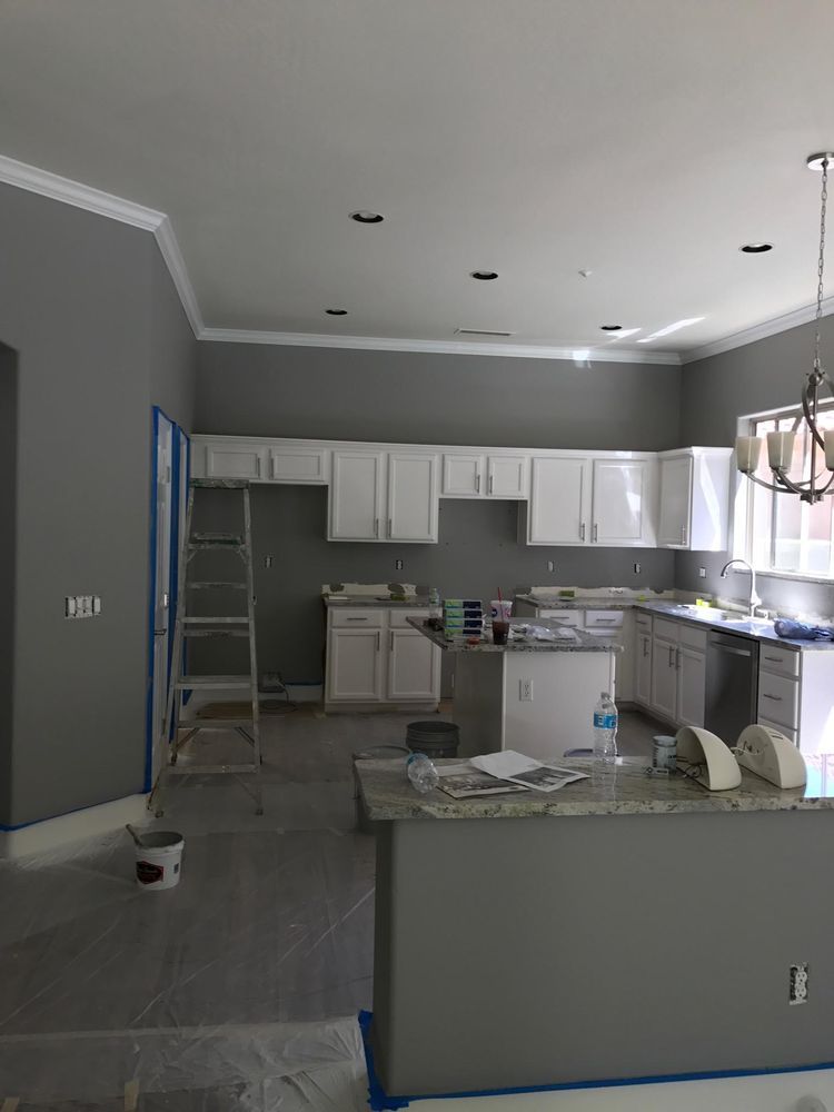 Kitchen renovation in progress, gray walls, white cabinets, island with granite countertop, ladder leaning against the wall.
