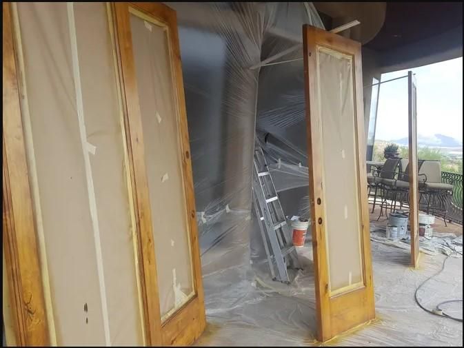 Two wooden doors leaned against a wall, prepared for painting. The glass is covered with paper and tape.