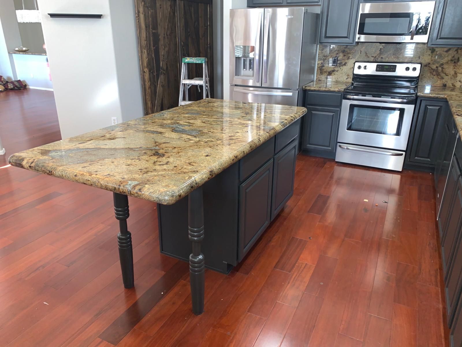 Kitchen with a granite countertop island and dark cabinets. Stainless steel appliances and hardwood floors.