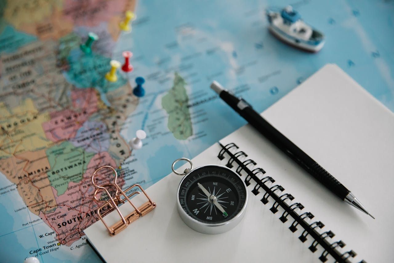 A compass , pen , and notebook are sitting on top of a map.