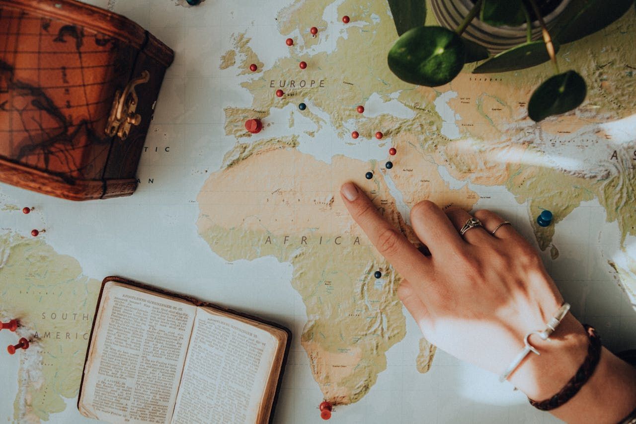 A person is pointing at a map of the world.
