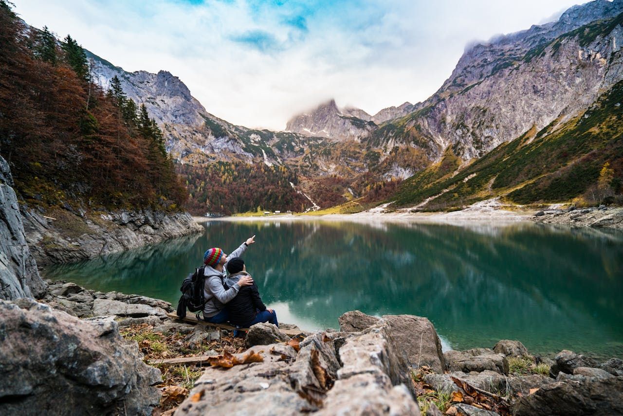 A couple is sitting on a rock near a lake in the mountains.
