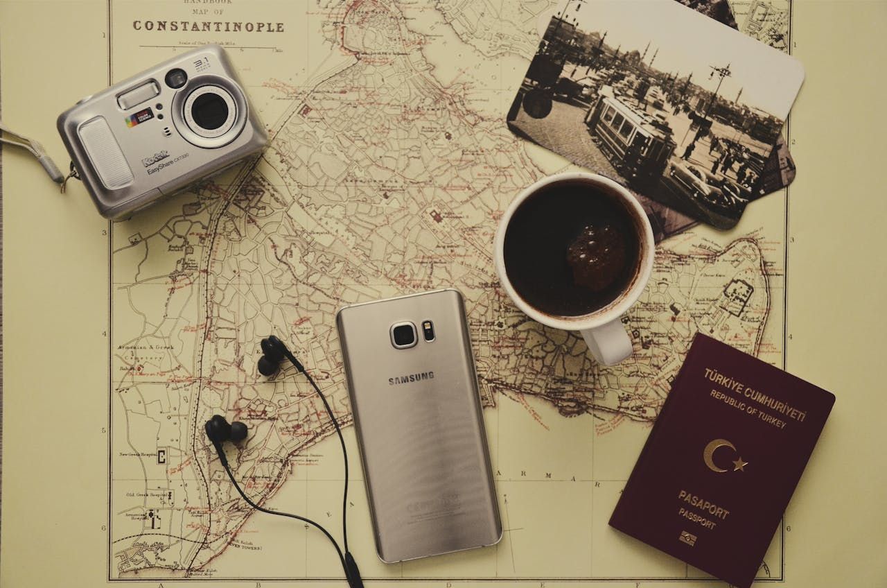 A camera , cell phone , passport , headphones and a cup of coffee on a map.