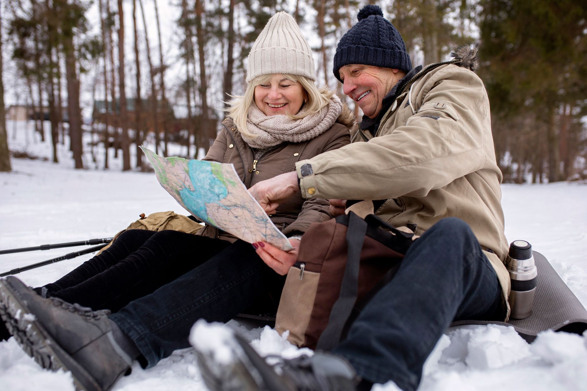 A man and a woman are sitting in the snow looking at a map.