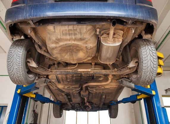 The underside of a car on a lift in a garage.